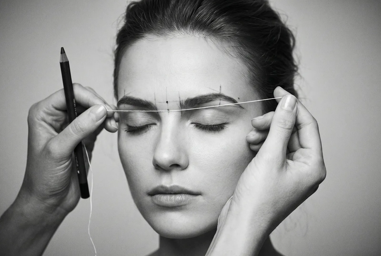 Brow artist using a mapping string and pencil to mark eyebrow points