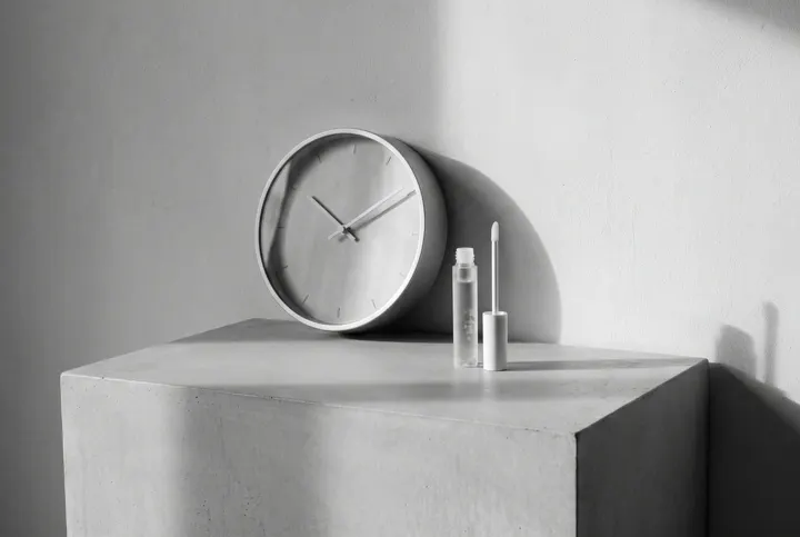 Minimal clock beside a brow serum on a plinth