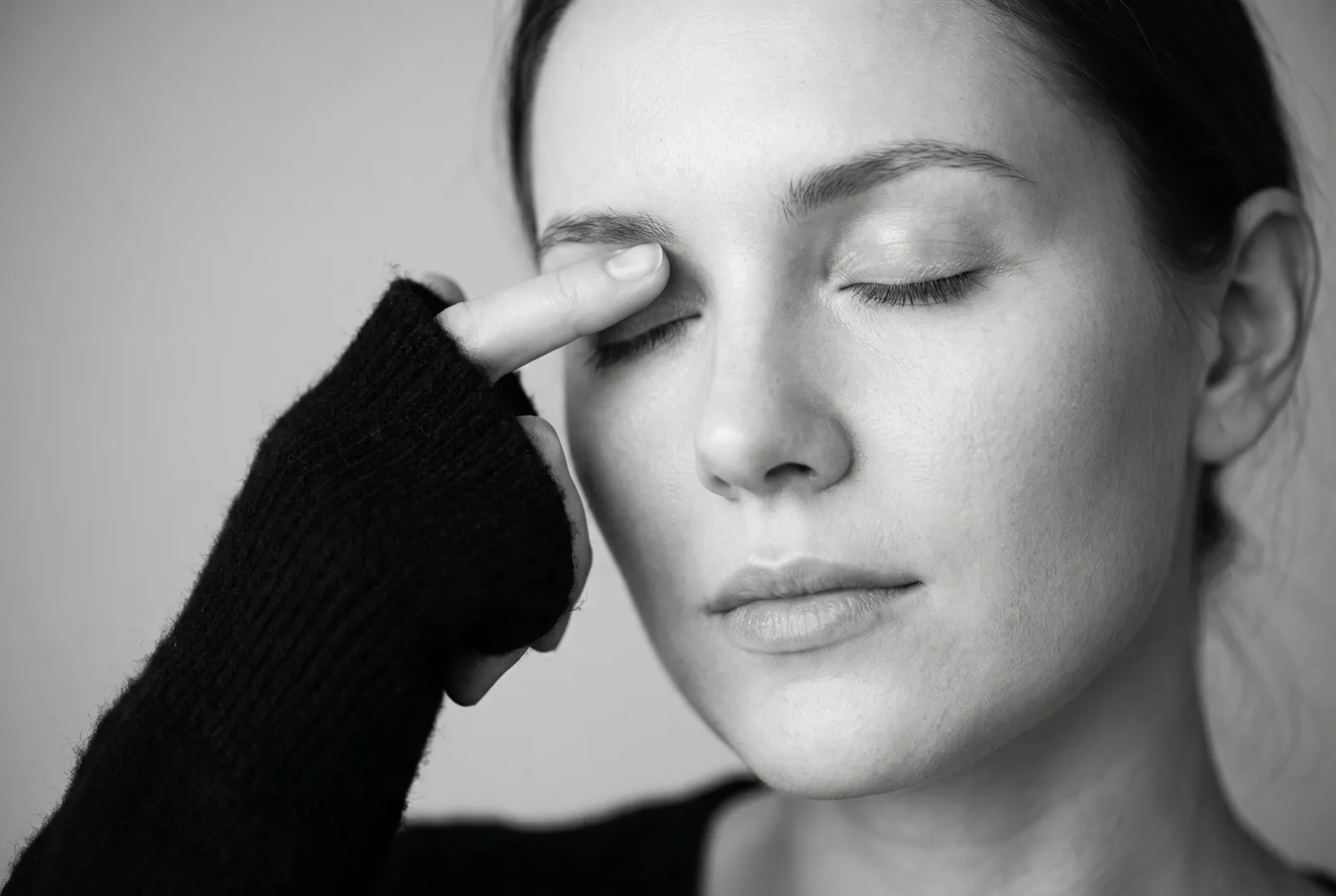 Woman with closed eyes gently touching her eyelid and brow area